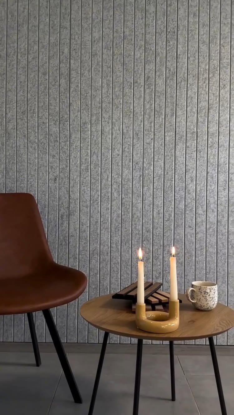 Grey vertical felt acoustic wall panels behind a brown chair and a small wooden table.