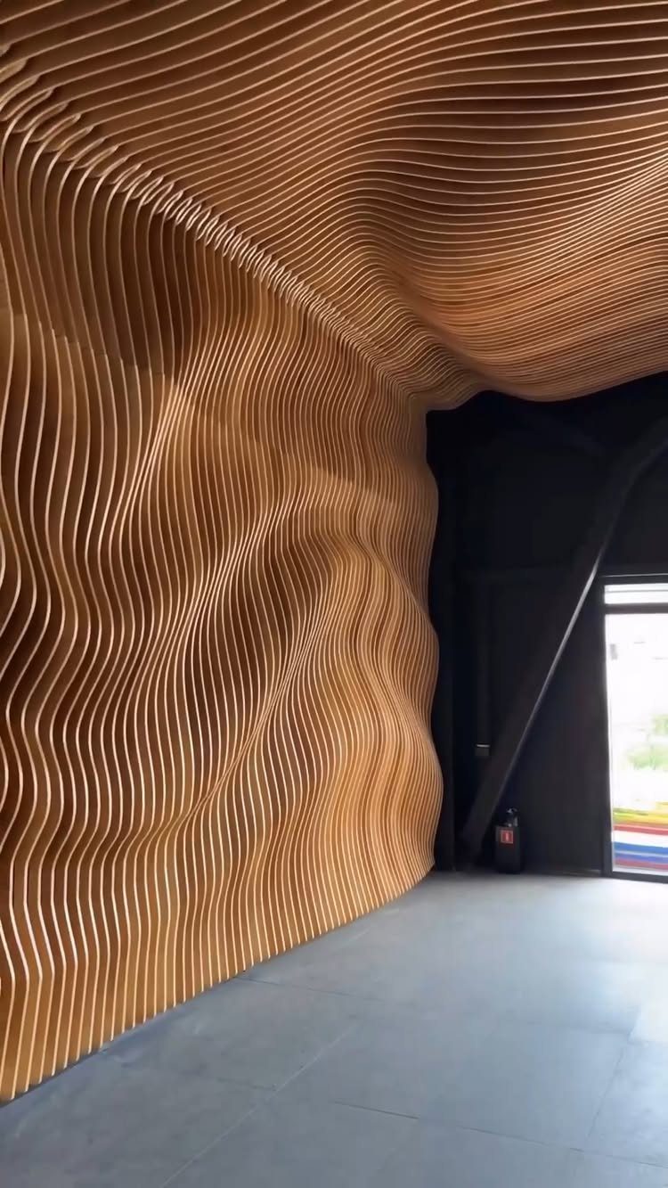 Wavy wooden slats forming an organic, undulating acoustic wall and ceiling installation in a room.
