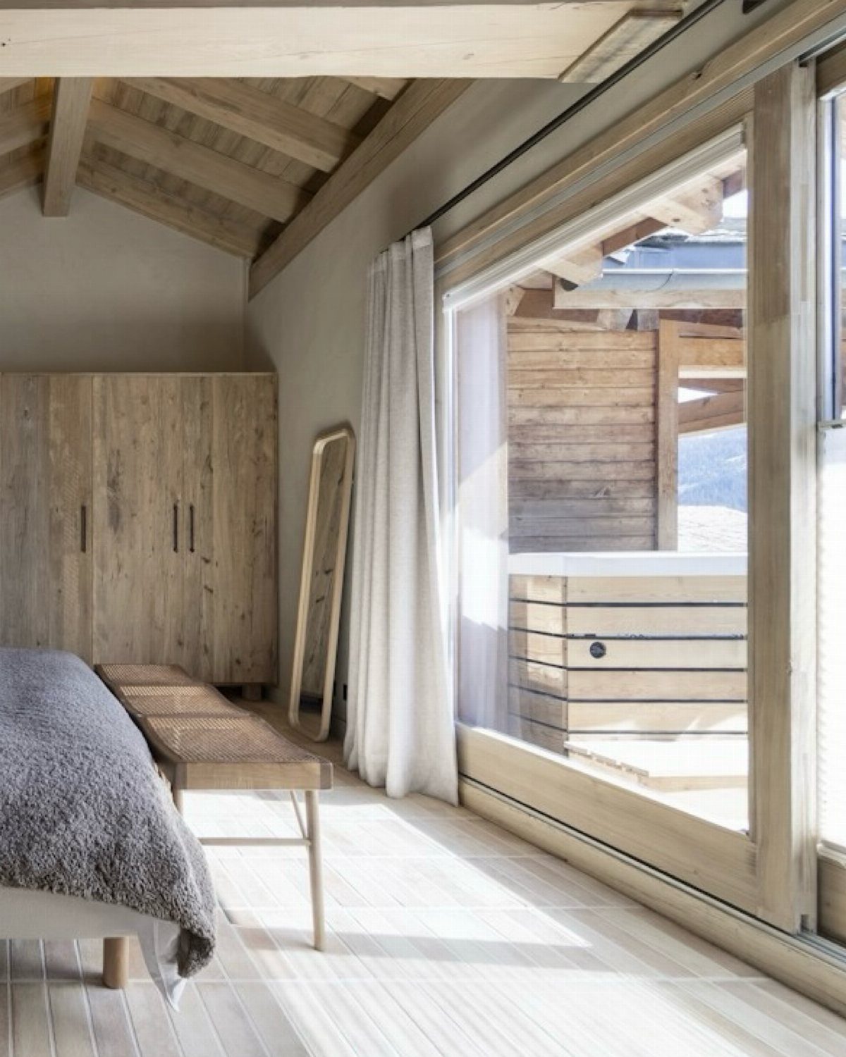 Light wood plank flooring in a bright bedroom with wooden furniture and large glass doors.