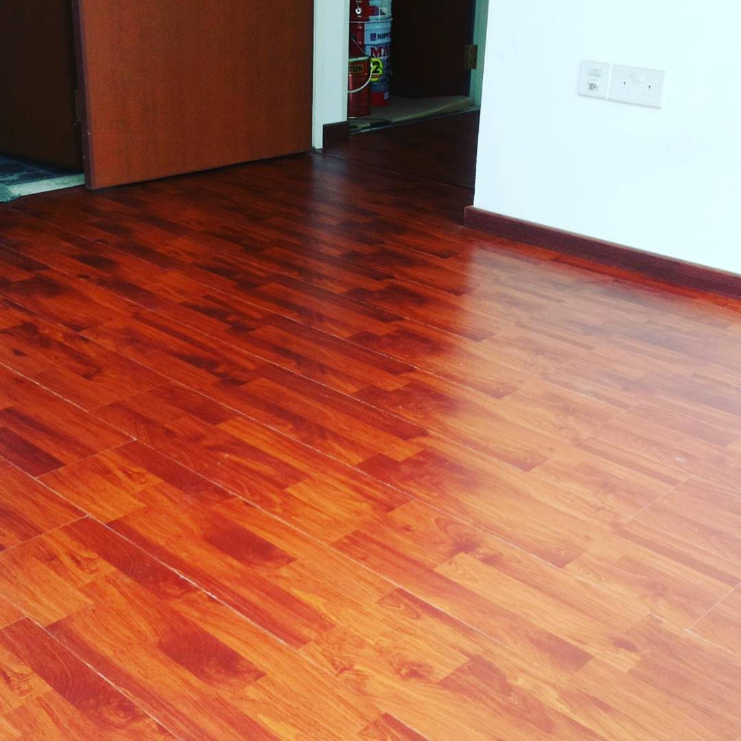Reddish-brown polished wood flooring in a room with white walls and a dark door.