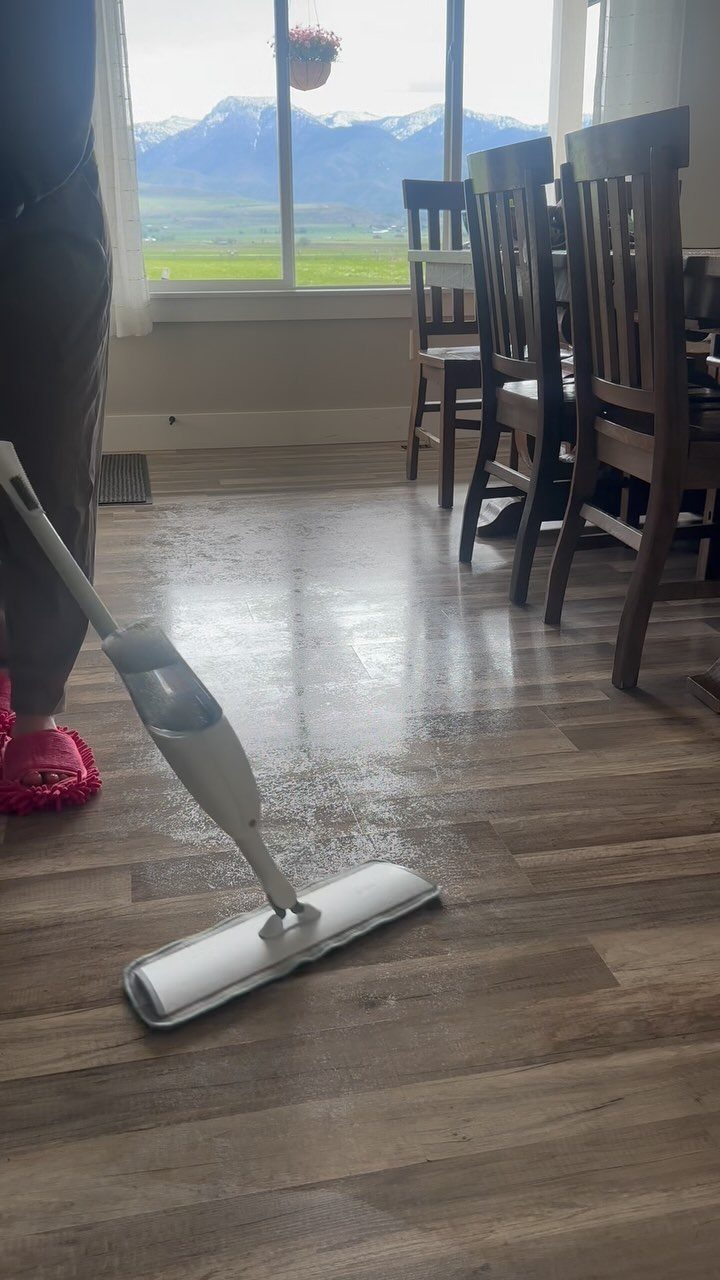 Aquaguard Laminate Flooring: 3 Easy Care Tips 1 A person using a white spray mop to clean a wood-look laminate floor near a dining table.