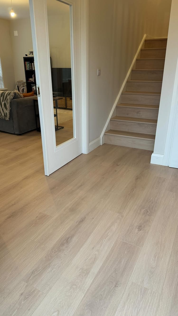 Aquaguard Laminate Flooring: 3 Easy Care Tips 2 Light wood-effect laminate flooring installed in a hallway and on a staircase next to a white door.