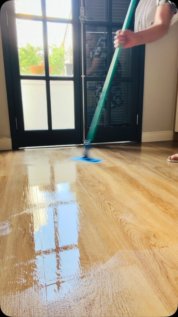 Aquaguard Laminate Flooring: 3 Easy Care Tips 3 A person using a green mop to clean a wet, reflective wood laminate floor.