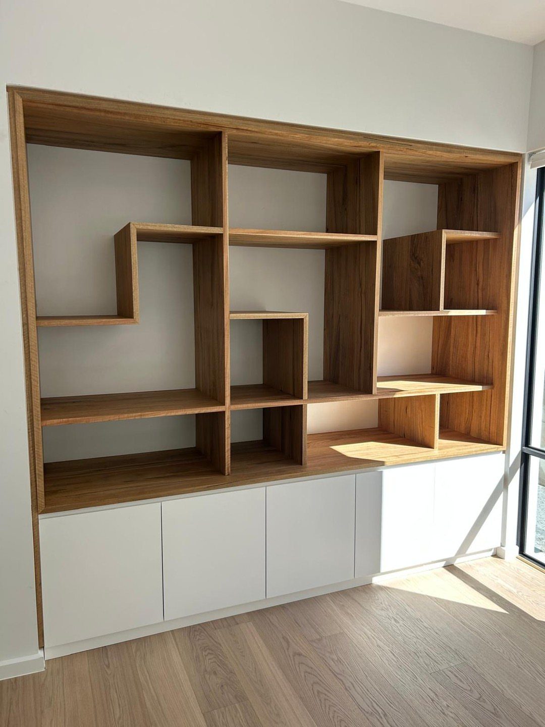 17 Built-In Shelves Living Room Ideas That Balance Style and Storage 12 Asymmetrical wooden built-in shelves with white lower cabinets against a white wall.