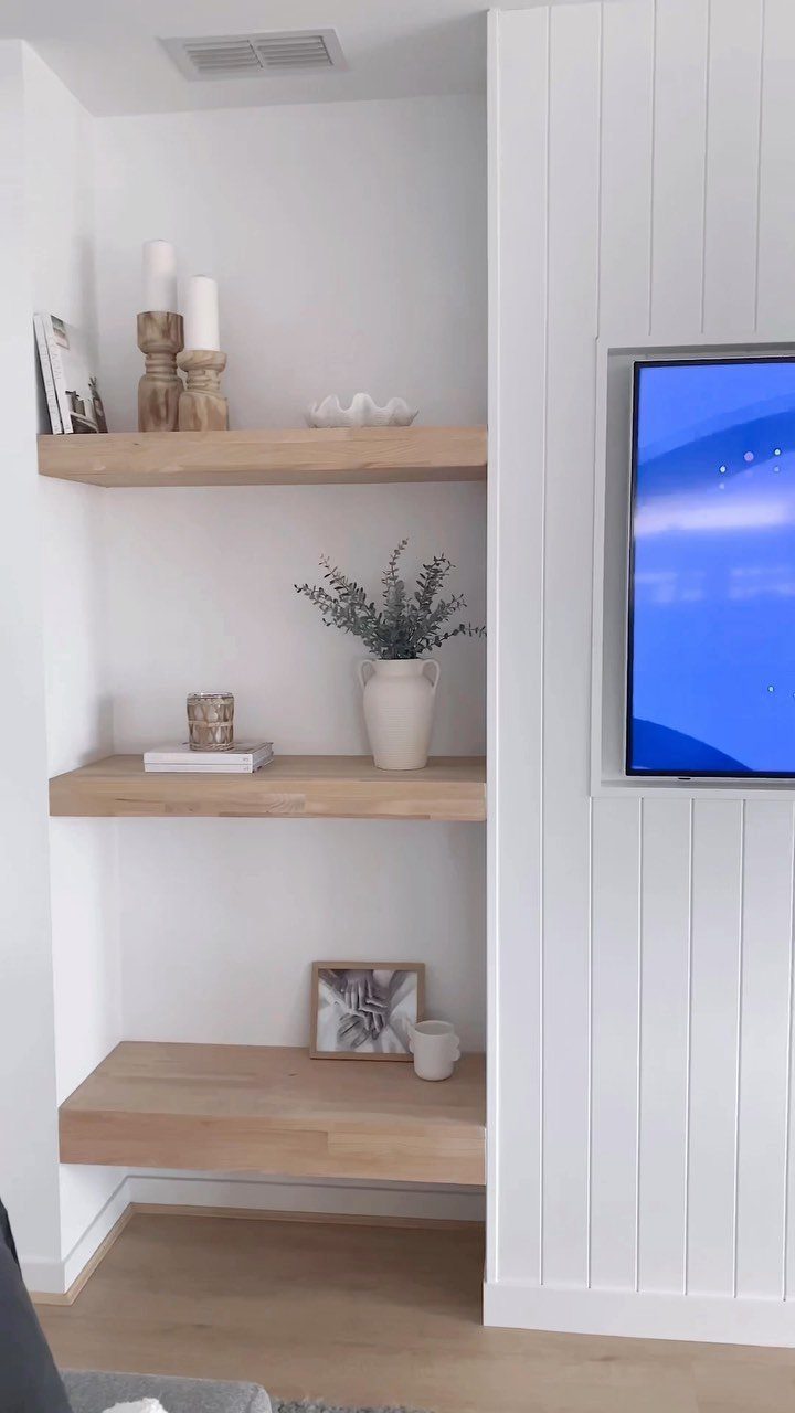 17 Built-In Shelves Living Room Ideas That Balance Style and Storage 10 White paneled wall with a recessed television and an alcove containing three light wood floating shelves.