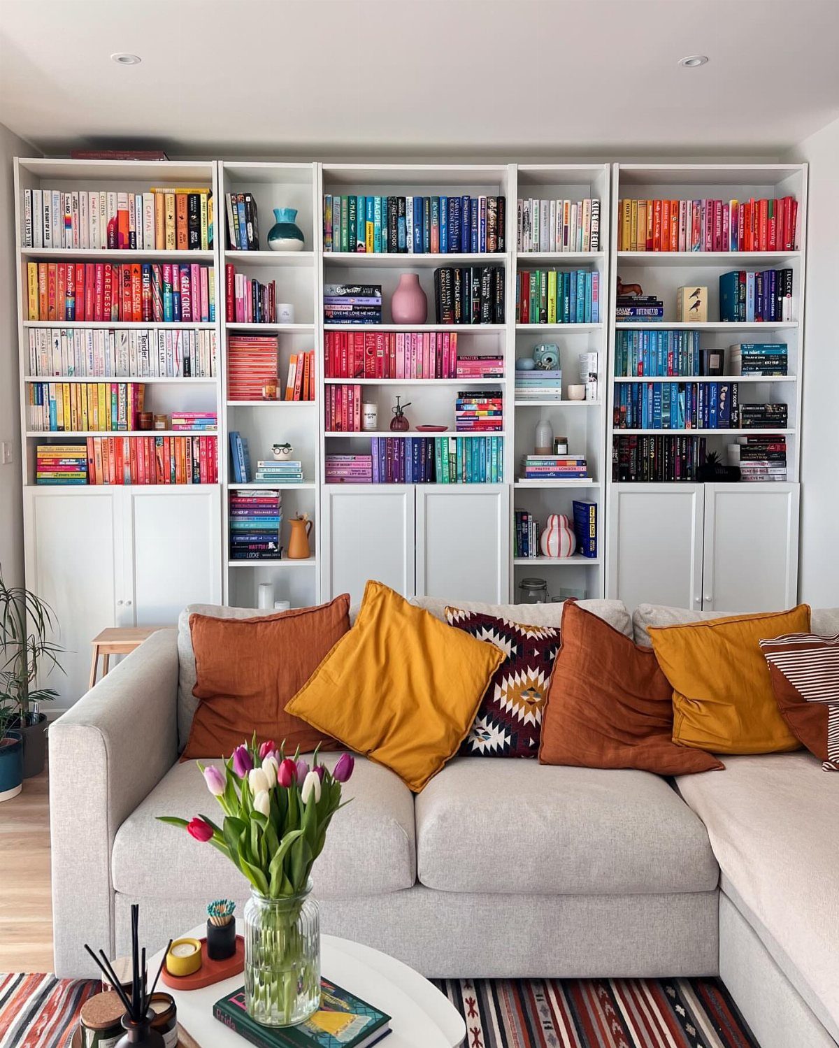 17 Built-In Shelves Living Room Ideas That Balance Style and Storage 15 White built-in bookshelves filled with colorful books behind a grey sofa with orange pillows.
