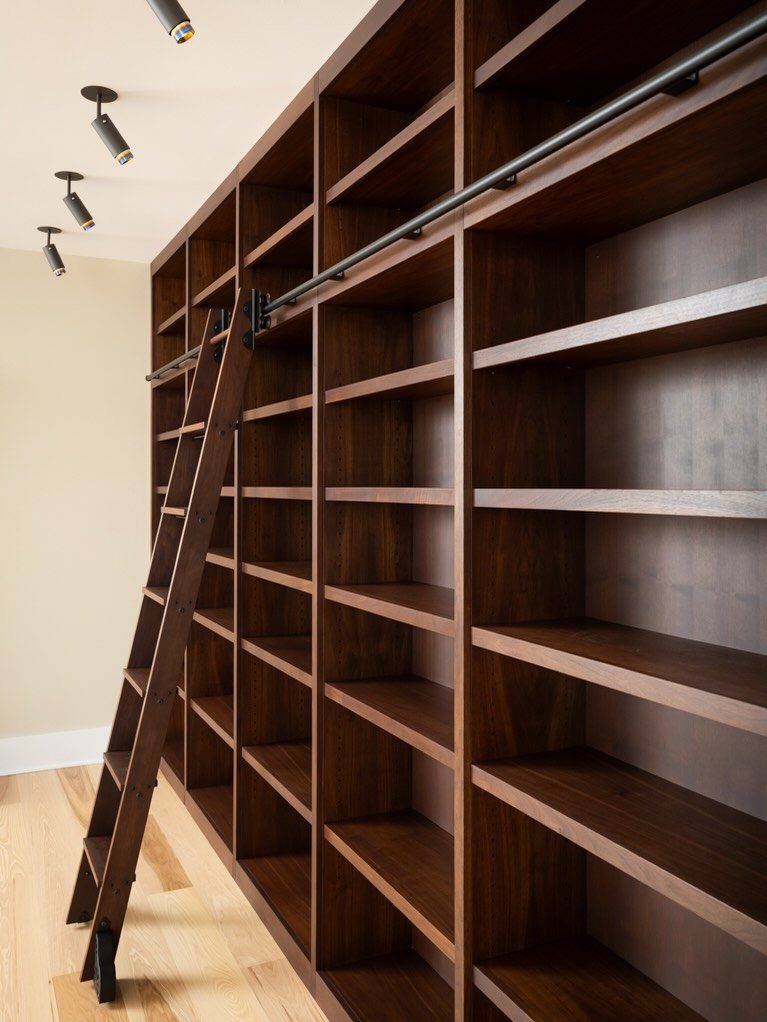 17 Built-In Shelves Living Room Ideas That Balance Style and Storage 16 Dark wood built-in bookshelves with a rolling wooden ladder on a black metal rail.