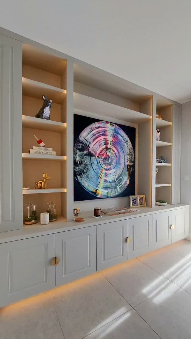 17 Built-In Shelves Living Room Ideas That Balance Style and Storage 2 Large light grey built-in shelving unit with illuminated compartments and lower cabinets in a bright room.