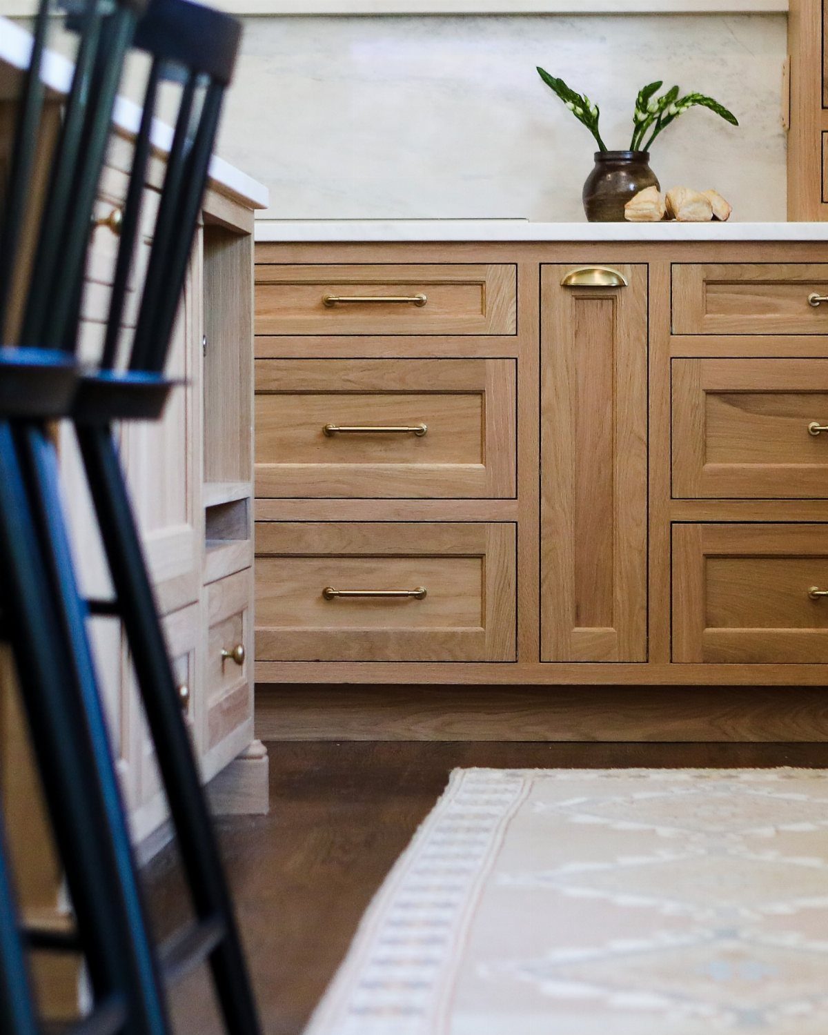 Dark Wood Floors with Light Wood Cabinets: 10 Kitchen Pairings 10 Light wood kitchen cabinets with gold handles sit above dark wood floors and a patterned rug.
