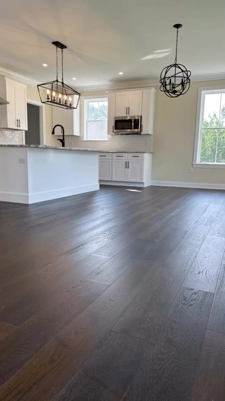 Fancy Wood Floors: 8 Ideas for Rich, Character-Filled Spaces 2 Dark wood plank flooring in a bright, modern kitchen with white cabinets and island.