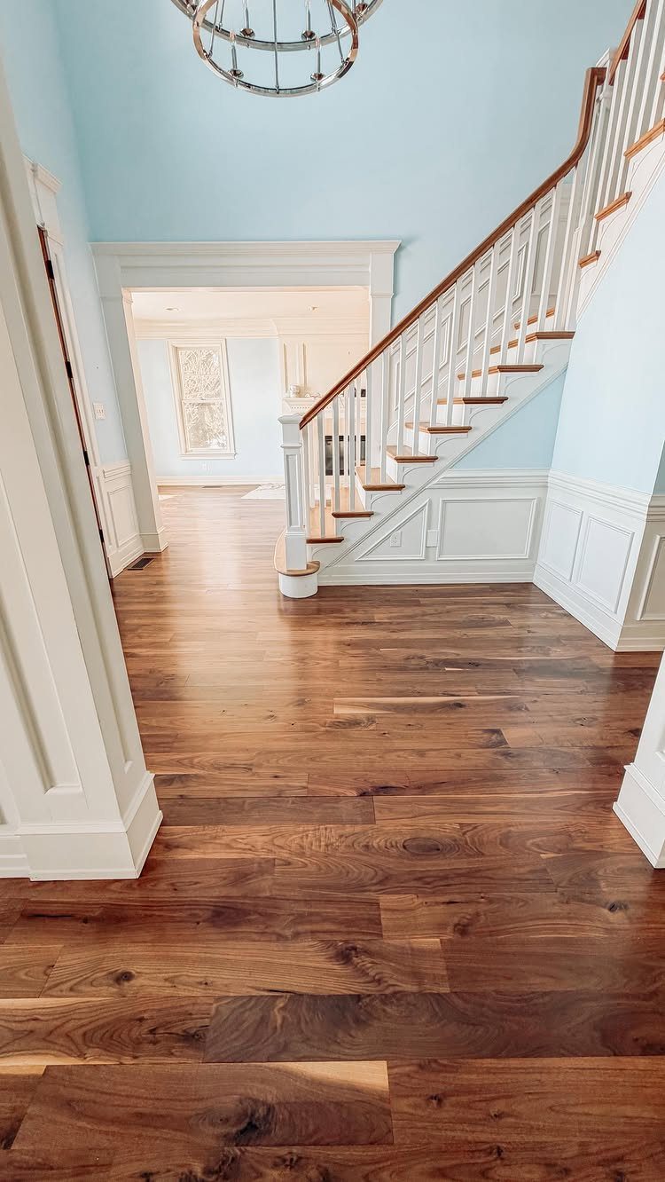 Fancy Wood Floors: 8 Ideas for Rich, Character-Filled Spaces 4 Dark walnut wood flooring planks in a bright hallway with a white staircase and blue walls.