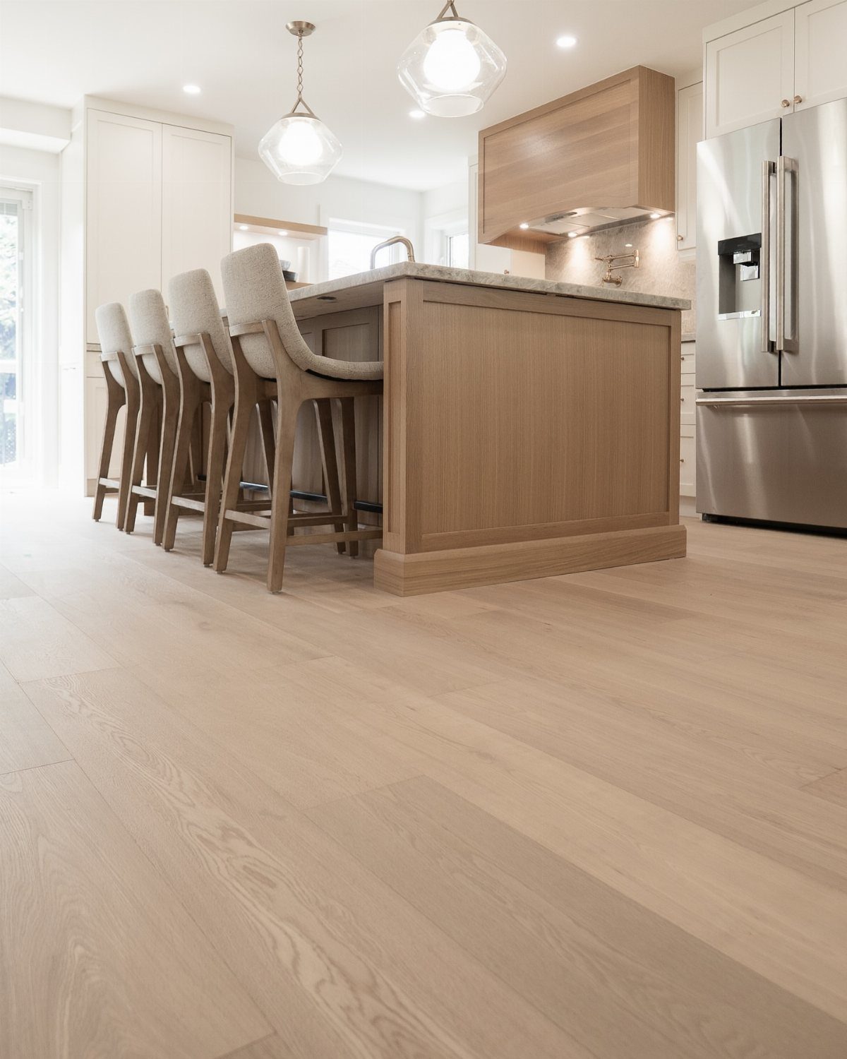 Fancy Wood Floors: 8 Ideas for Rich, Character-Filled Spaces 5 Light wood plank flooring in a bright, modern kitchen with a wooden island and bar stools.