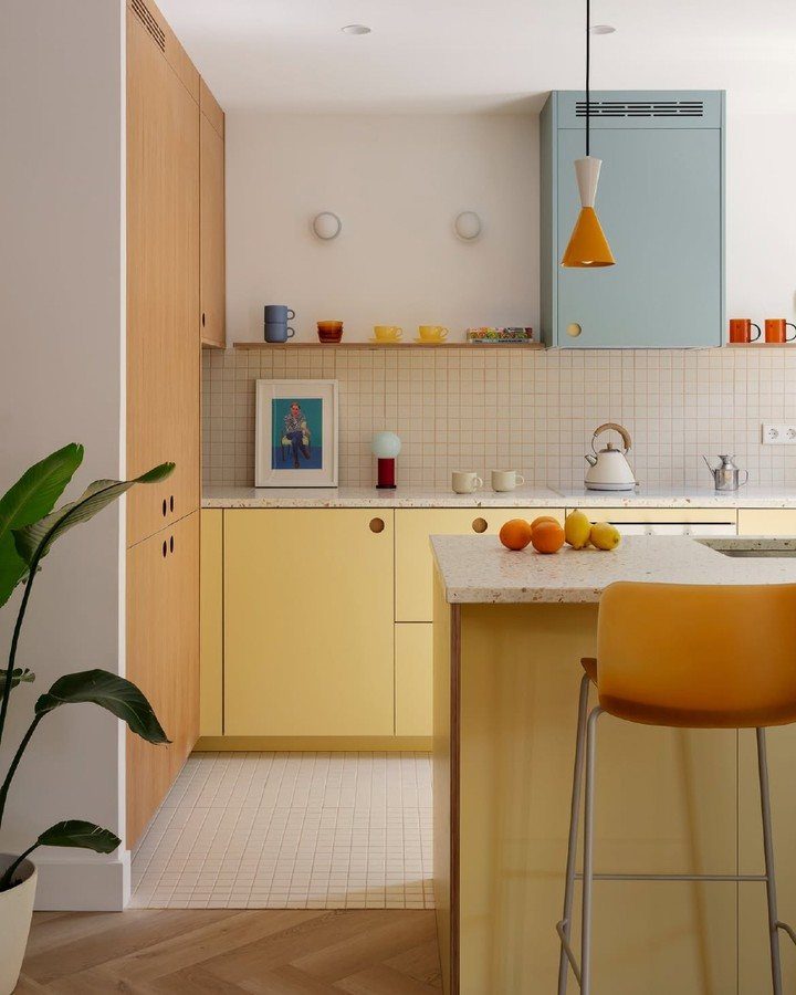 Kitchen Floors with Wood Cabinets: 10 Ideas That Work 3 Yellow and blue kitchen cabinets with colorful mugs and citrus fruits on a white countertop.