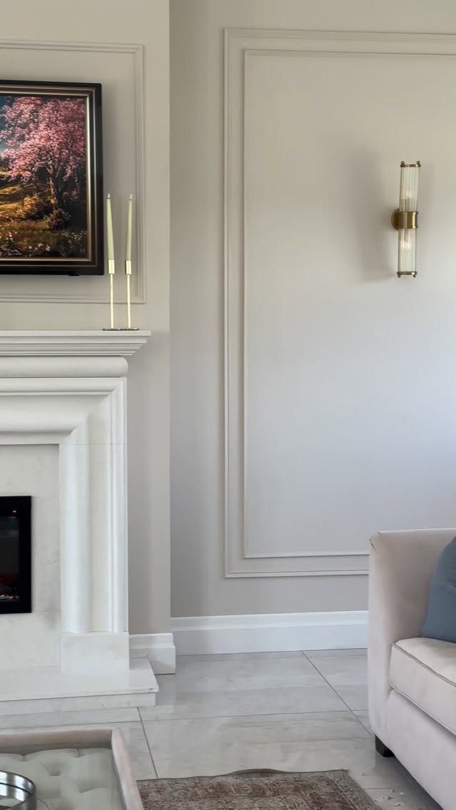Decorative rectangular wall moldings on a beige wall next to a white marble fireplace.