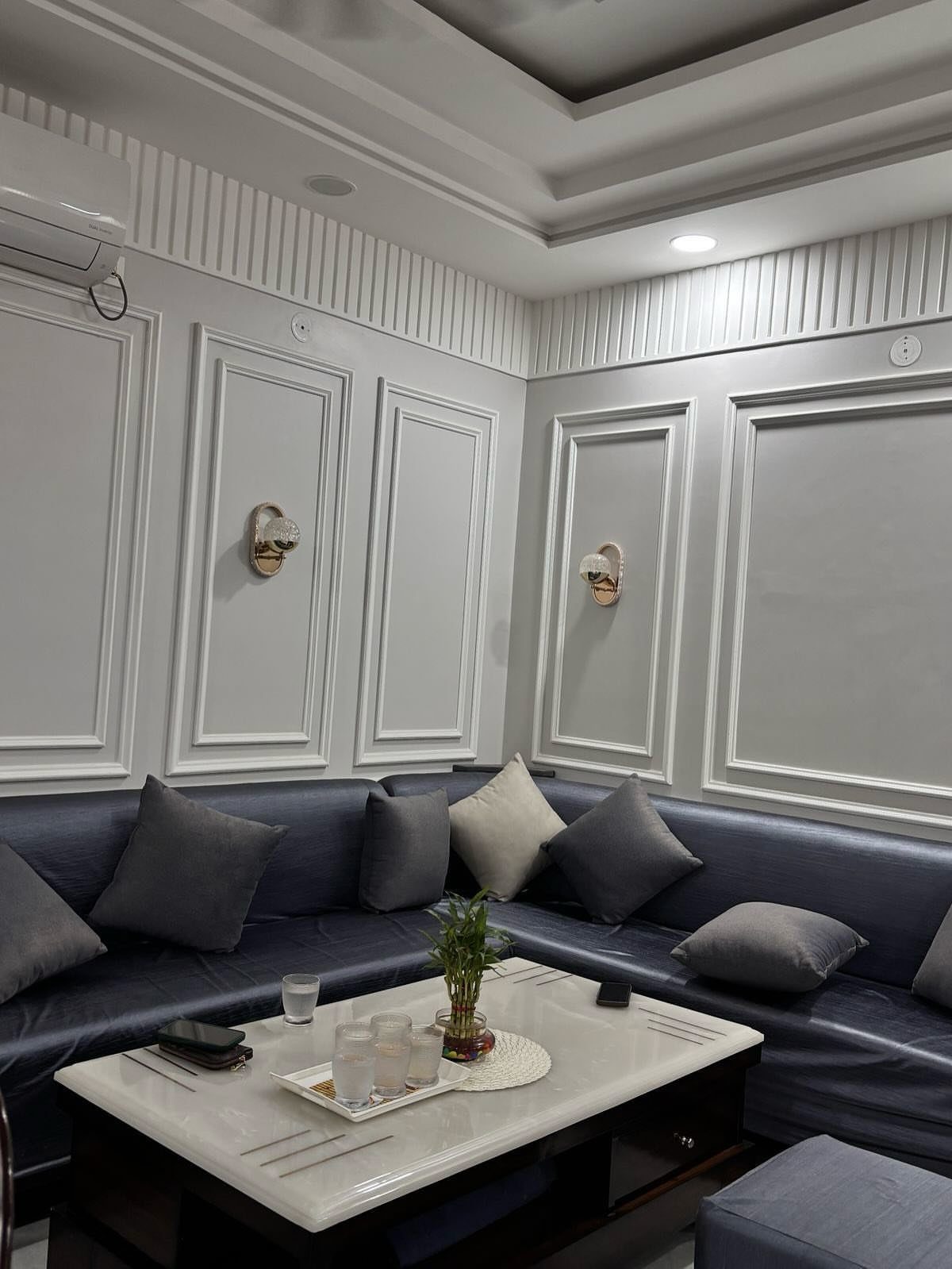 Grey walls with white decorative rectangular molding panels above a blue sectional sofa.