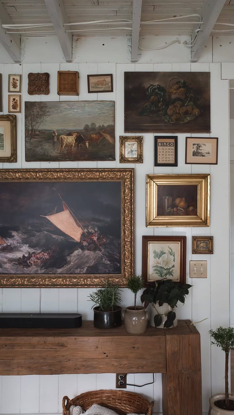 Framed landscape and seascape paintings arranged in a gallery wall style on a white paneled wall.