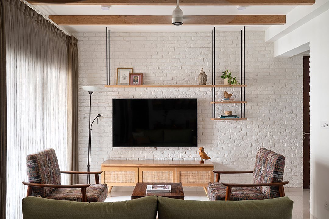 A black television mounted on a white painted brick wall with wooden shelves and furniture.