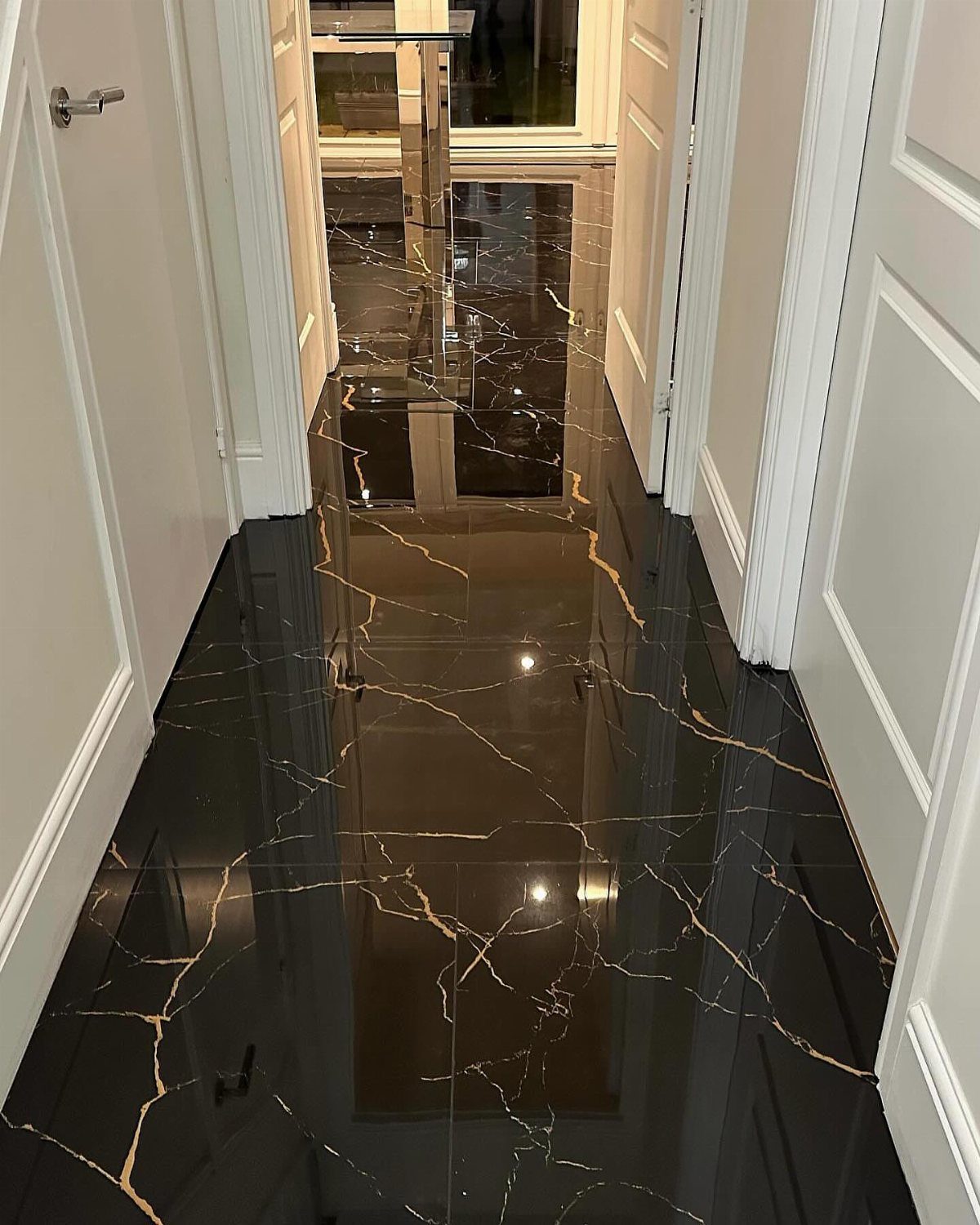 Polished black marble flooring with gold veining running through a narrow white hallway.