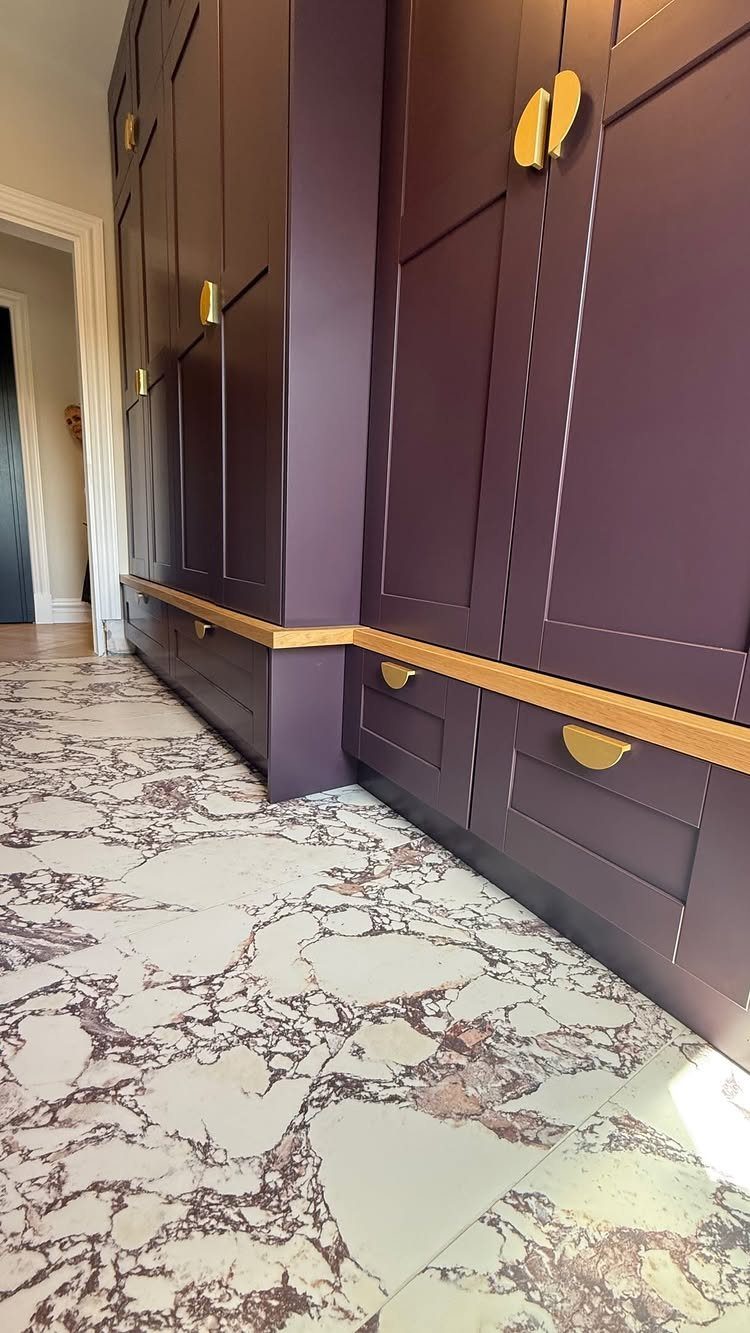 White marble floor with dramatic dark veining running alongside dark purple cabinetry.