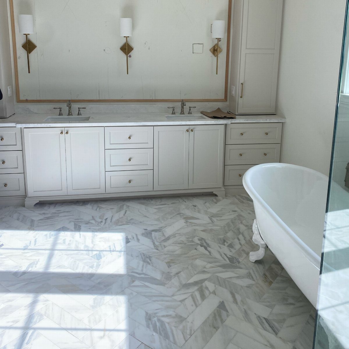 White marble tiles in a herringbone pattern covering a bright, modern bathroom floor.
