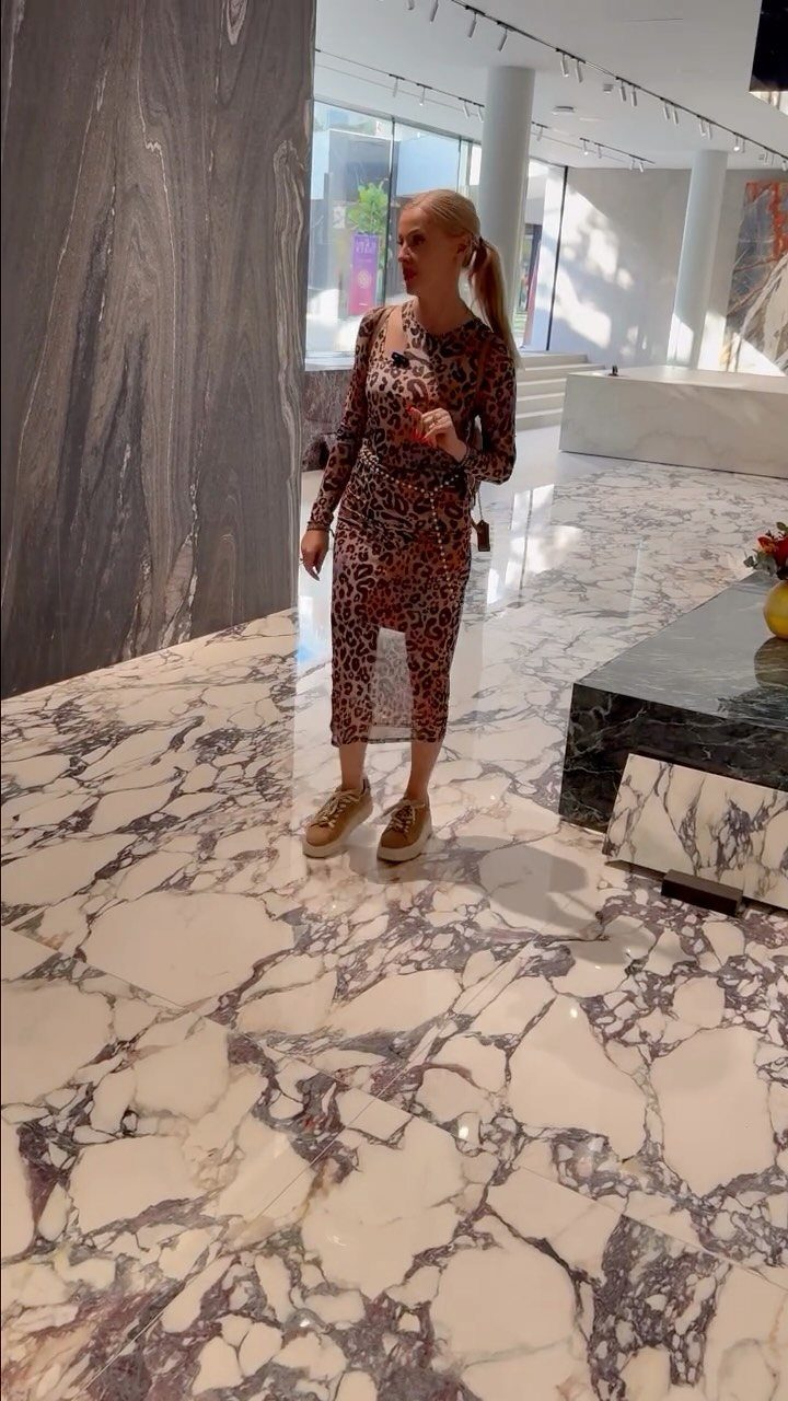Woman standing on a polished white marble floor with large purple and grey veins.