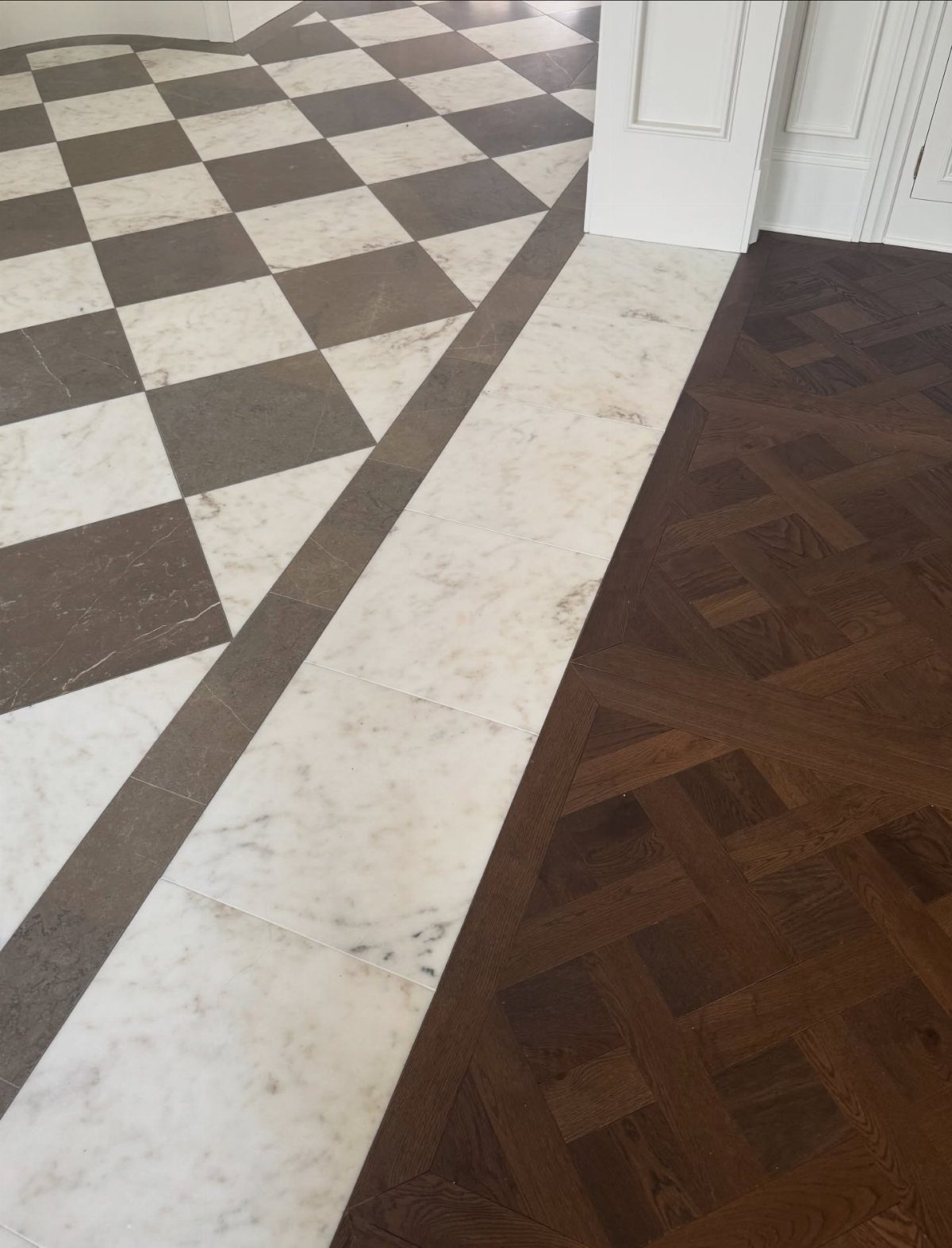 Checkered black and white marble tiles meeting a white marble border and dark wood parquet flooring.