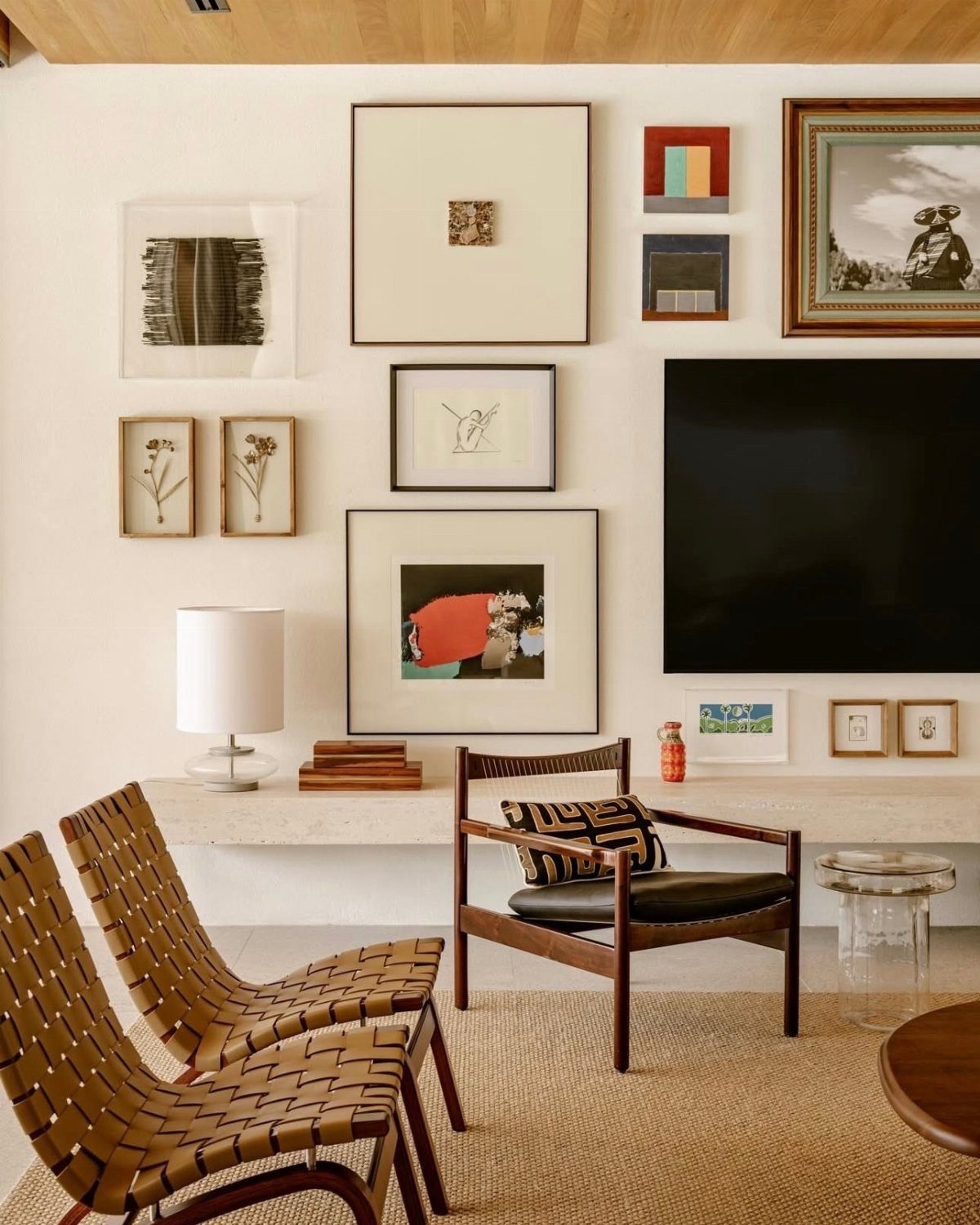 Framed art pieces arranged on a white wall around a large black television screen.