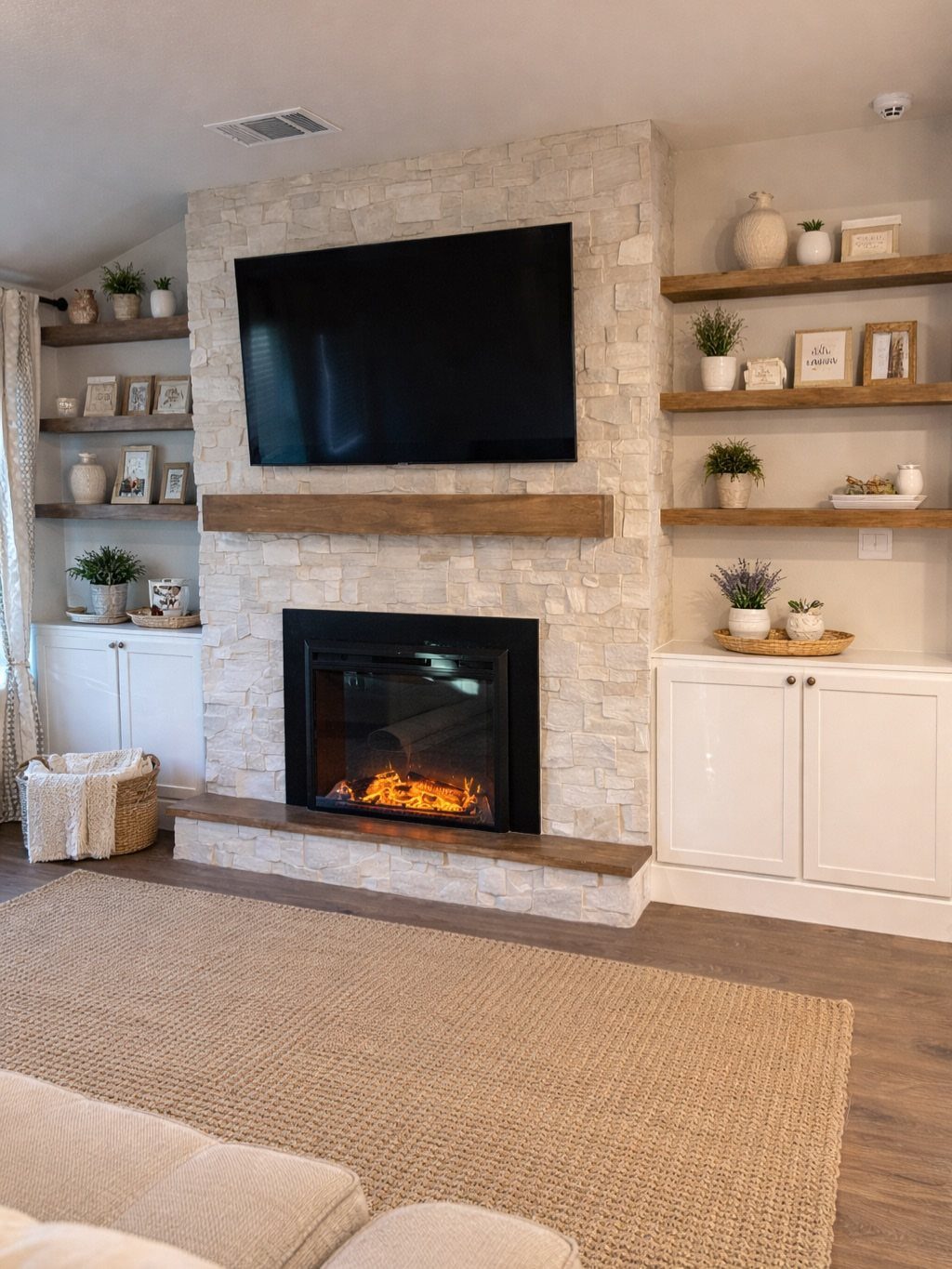 Stone media wall with an electric fireplace, mounted TV, wooden mantel, and floating shelves.