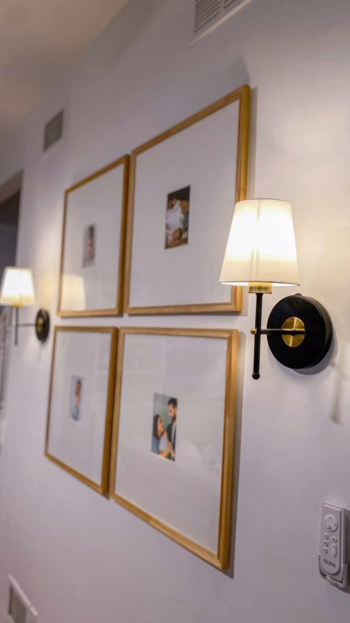 Four gold-framed photos arranged in a grid on a white wall with warm sconce lighting.