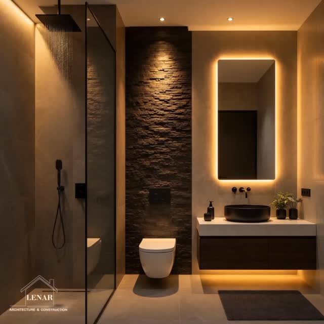 Modern bathroom featuring a dark stone textured accent wall, glass shower, and backlit mirror.