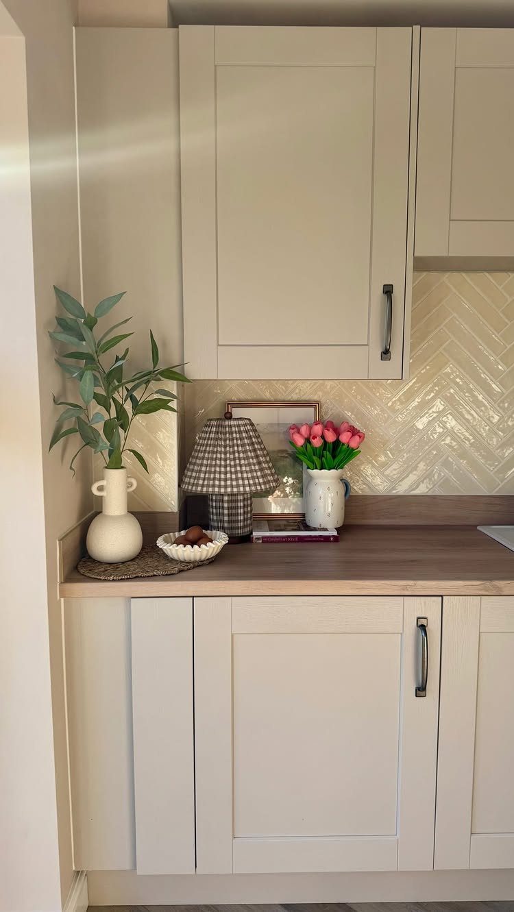 Cream herringbone subway tile backsplash behind a kitchen countertop with beige cabinets and decorative items.