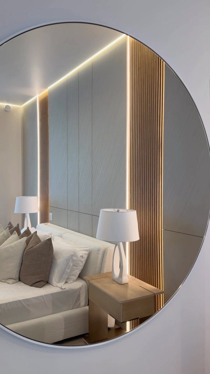 Circular mirror reflecting a modern bedroom with grey paneled walls and warm LED lighting.