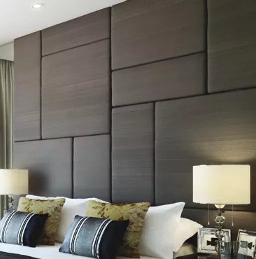 Dark grey upholstered rectangular panels arranged geometrically as a bedroom accent wall behind a bed.