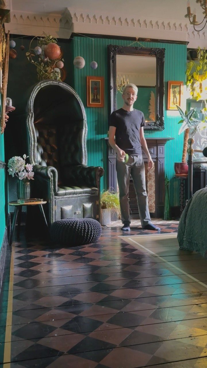 5 Painted Wood Floors for Pattern, Pale Color, and Bold Graphics 1 A man stands in a room with teal walls and a checkerboard patterned wood floor.