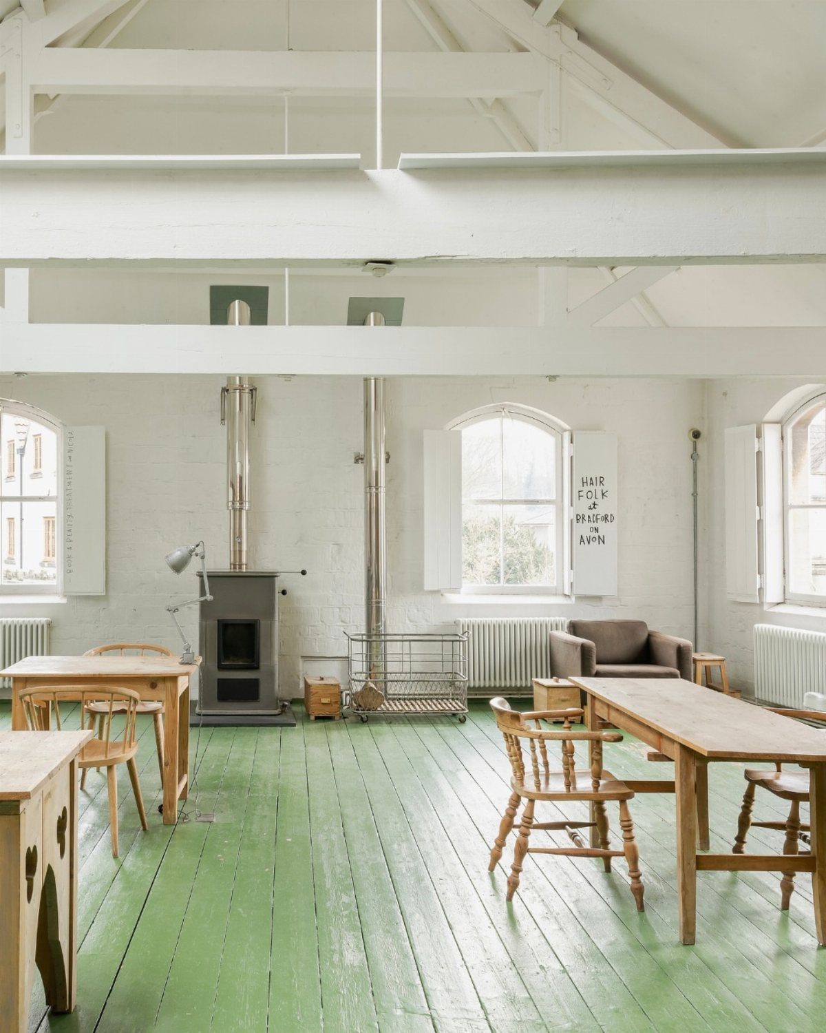 5 Painted Wood Floors for Pattern, Pale Color, and Bold Graphics 3 Green painted wooden floorboards in a bright, white-walled room with wooden furniture and a wood-burning stove.