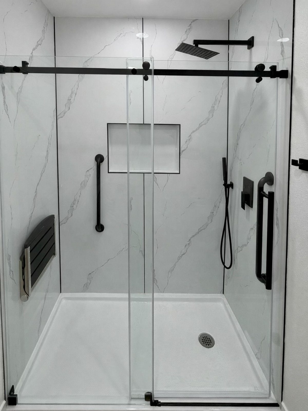 A modern walk-in shower featuring white marble-patterned wall panels and black hardware.