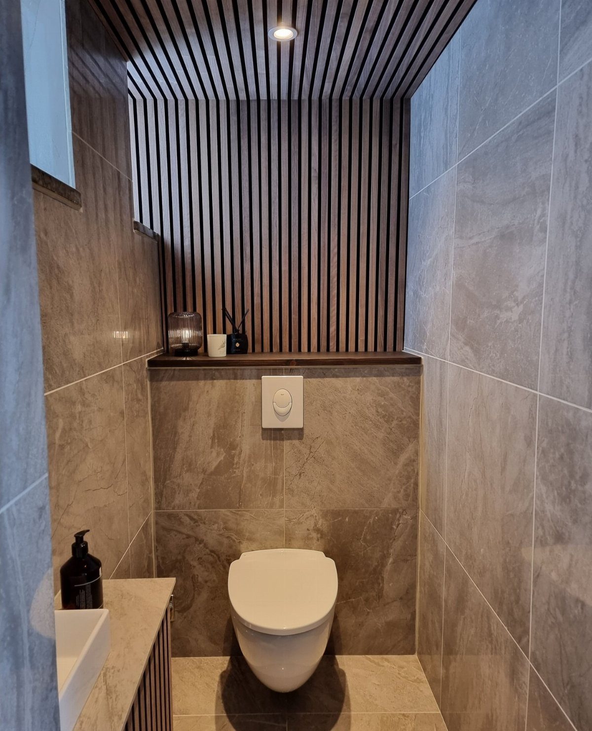 Vertical dark wood slats covering a bathroom wall and ceiling behind a white toilet.