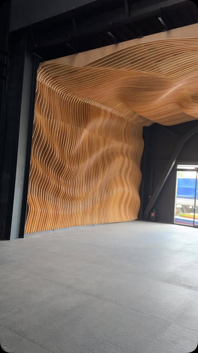 12 Plywood Wall Ideas for Living Rooms, Offices and Bedrooms 6 Undulating wooden slat wall forming a large, sculptural curved structure in a dark room.