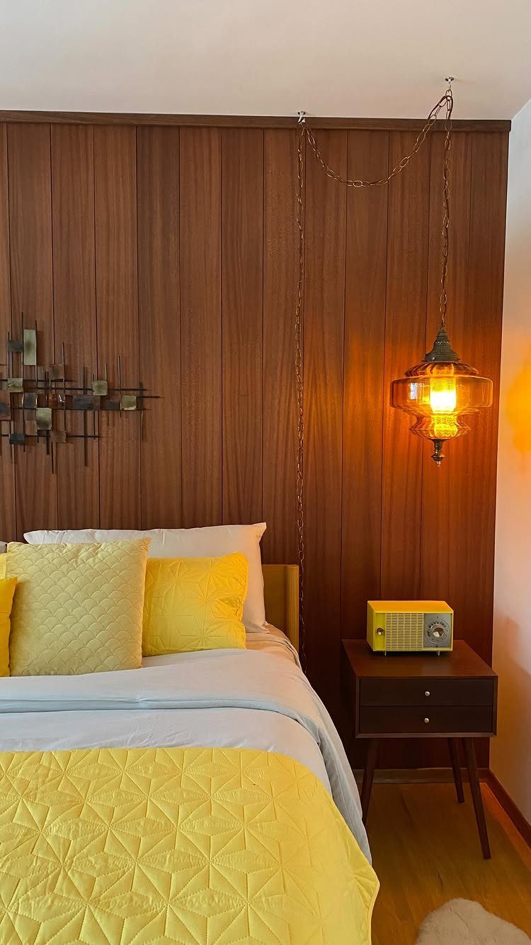 12 Plywood Wall Ideas for Living Rooms, Offices and Bedrooms 4 Vertical grooved plywood wall panels behind a bed with yellow bedding and an amber lamp.