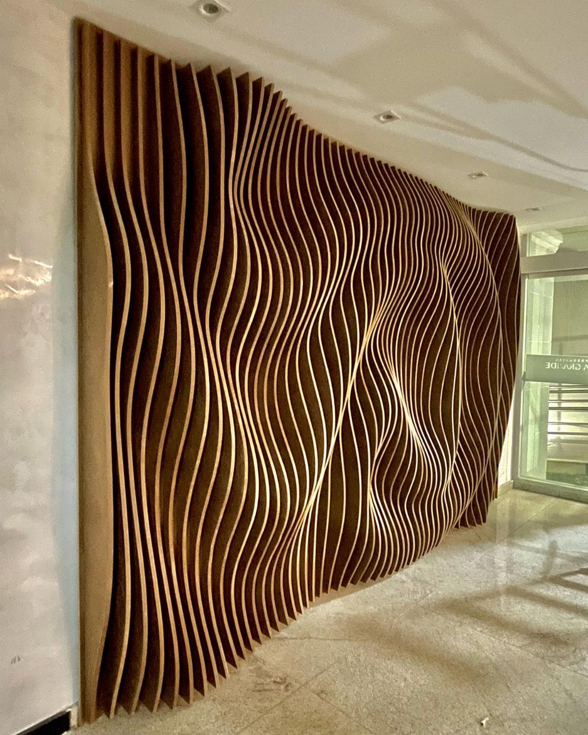 12 Plywood Wall Ideas for Living Rooms, Offices and Bedrooms 7 Wavy vertical plywood slats forming a large sculptural three-dimensional wall feature in a modern room.