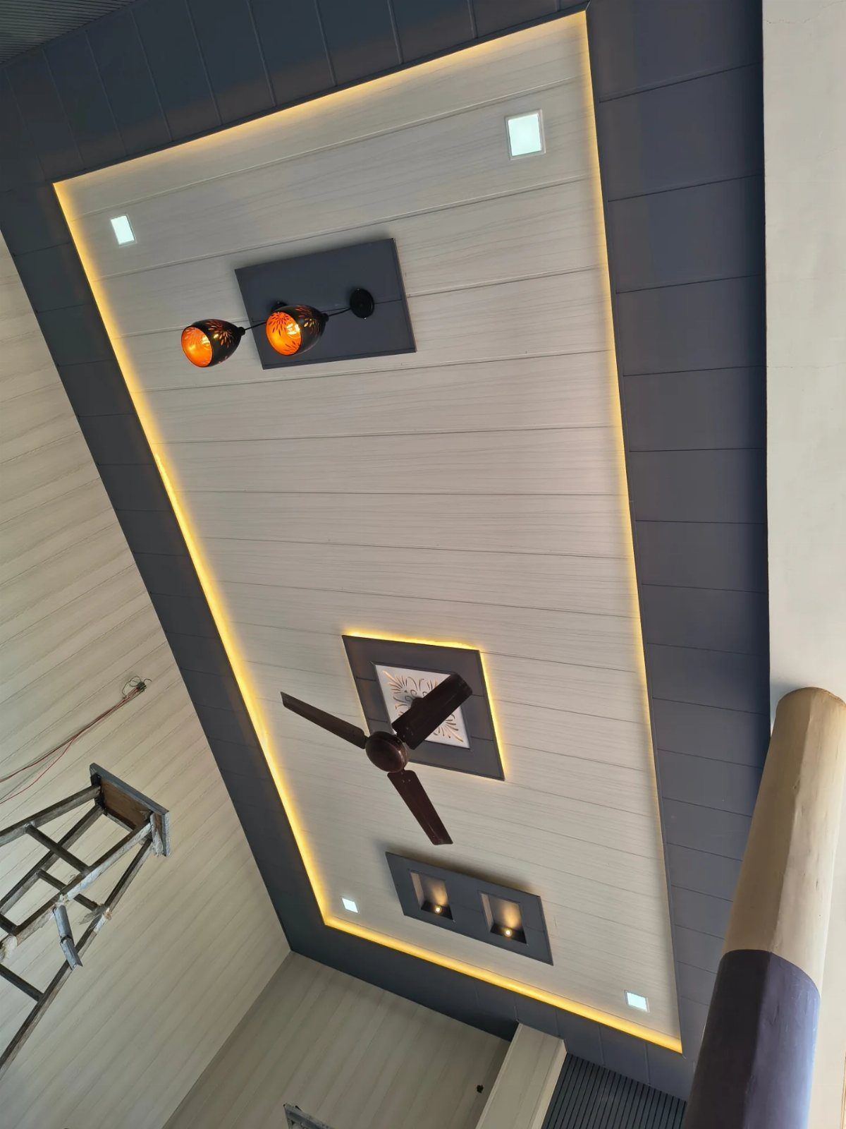 PVC Panel Design: 9 Ideas for Walls, Ceilings and Exteriors 1 White paneled ceiling with dark grey borders, recessed lights, and a ceiling fan.