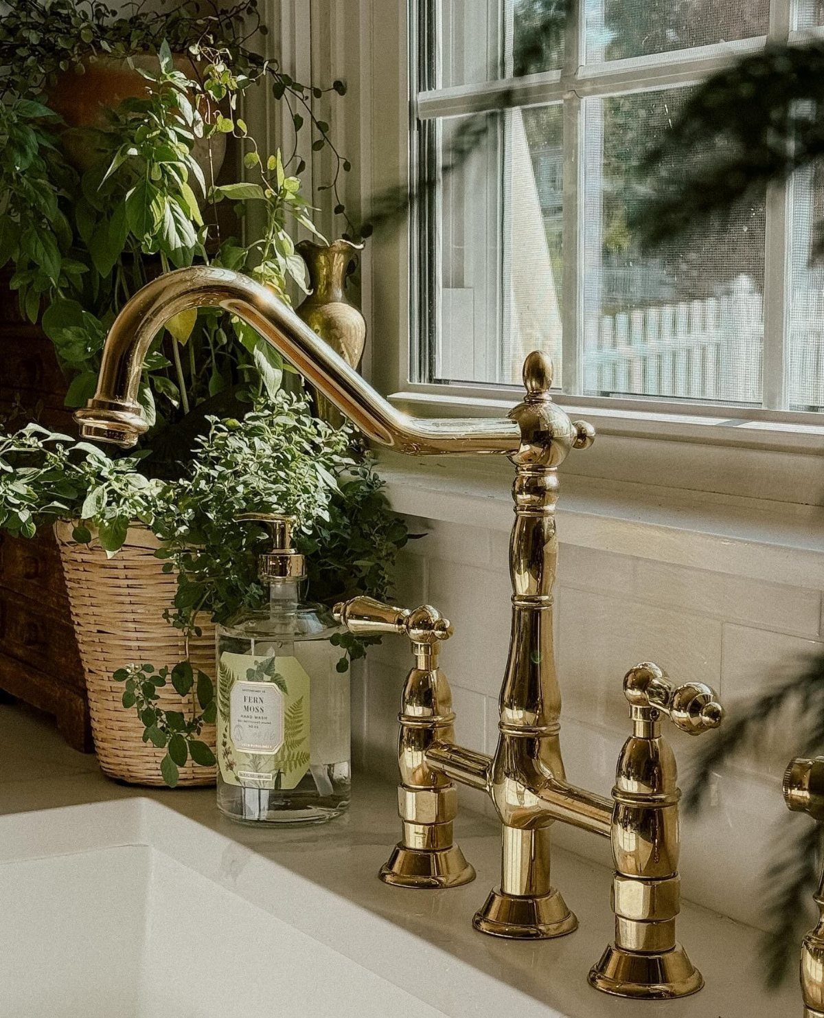 29 Rustic Farmhouse Kitchen Ideas That Feel Collected, Not Cataloged 3 Gold farmhouse-style faucet with dual handles installed on a white kitchen countertop near a window.
