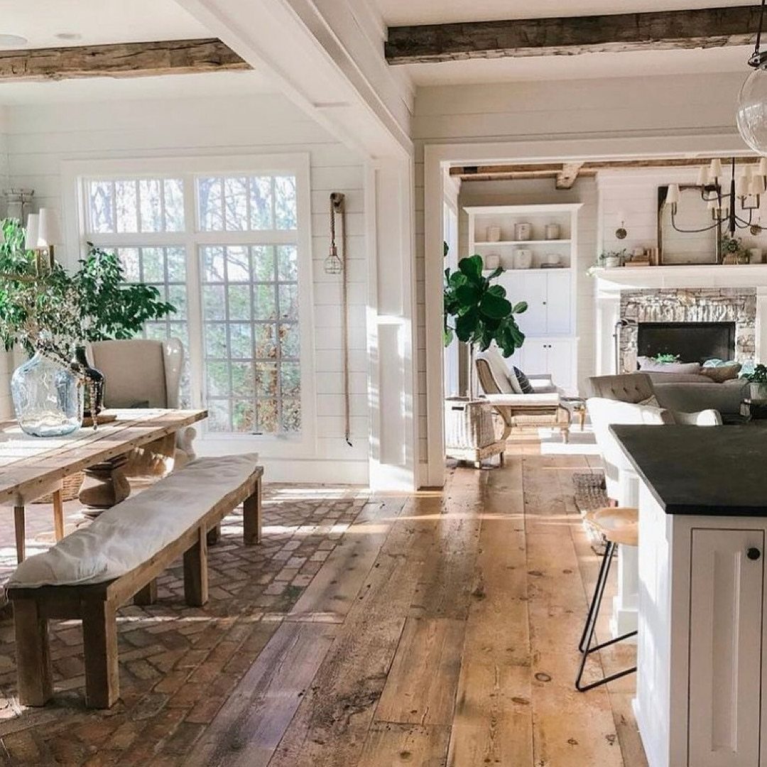 29 Rustic Farmhouse Kitchen Ideas That Feel Collected, Not Cataloged 7 Wooden dining table and bench in a bright room leading into a rustic kitchen.