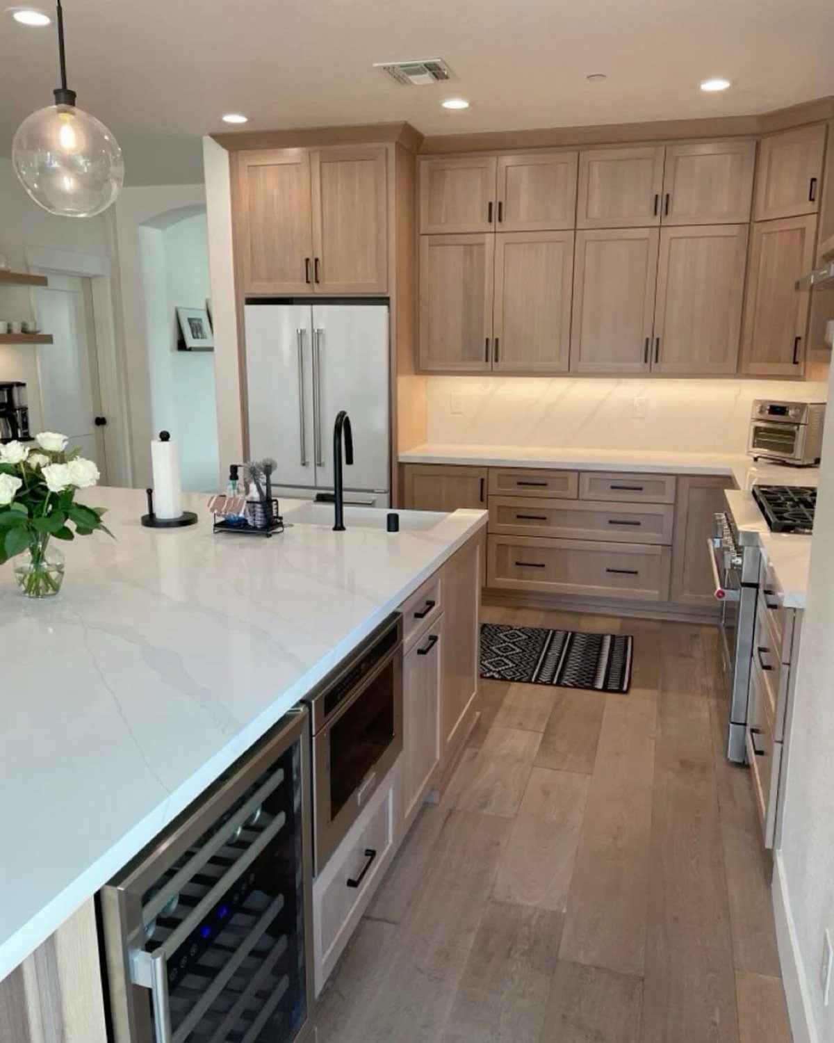 29 Rustic Farmhouse Kitchen Ideas That Feel Collected, Not Cataloged 15 Light wood Shaker-style kitchen cabinets with white quartz countertops and a large central island.