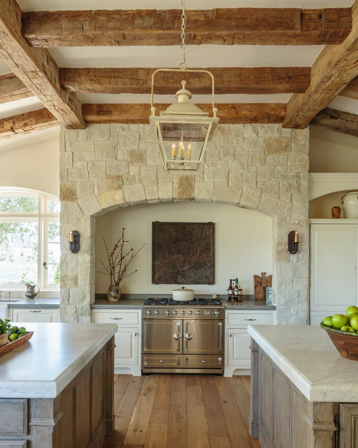 29 Rustic Farmhouse Kitchen Ideas That Feel Collected, Not Cataloged 26 Rustic kitchen with stone archway, wooden ceiling beams, and marble countertops.