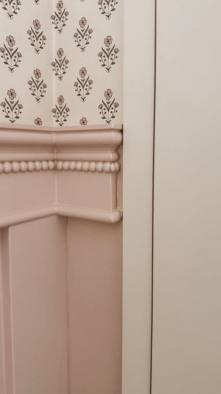 Decorative pink chair rail moulding separating floral wallpaper from vertical wall paneling.
