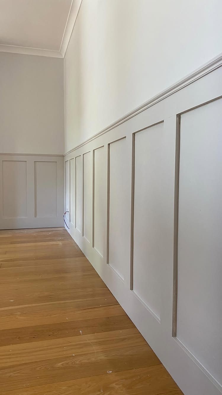 White wainscoting with rectangular panel moulding installed on a wall above light wood flooring.