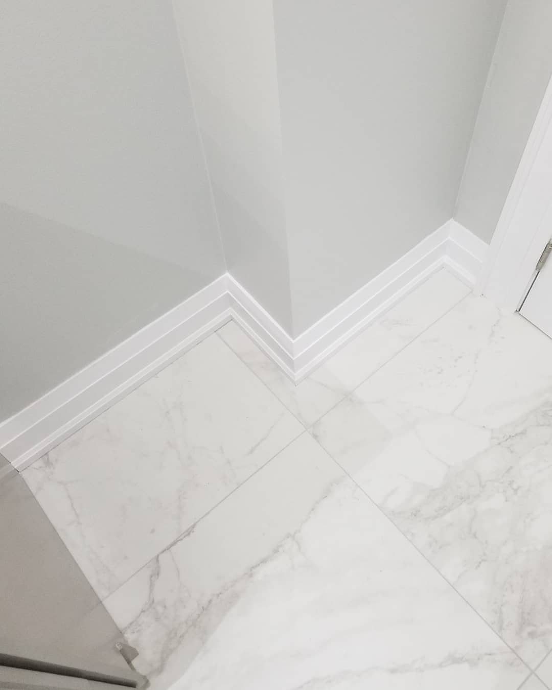 Trim Work on Walls: 8 Styles That Add Detail to Any Room 3 White baseboard molding installed along light grey walls meeting a marble tiled floor in a corner.