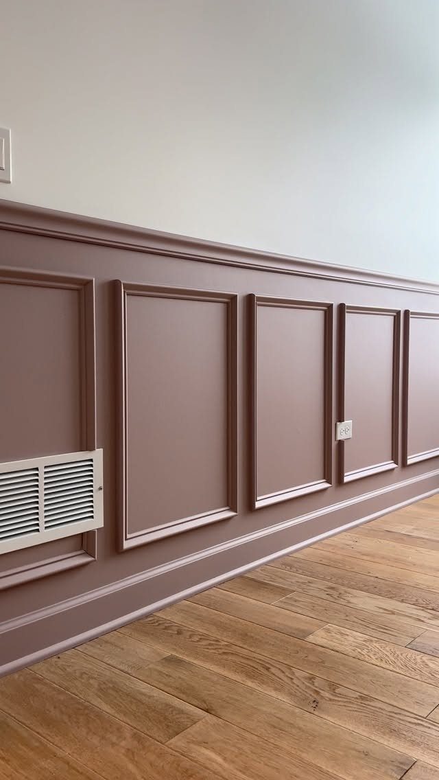 Mauve wainscoting with rectangular molding panels installed on a wall above light wood flooring.