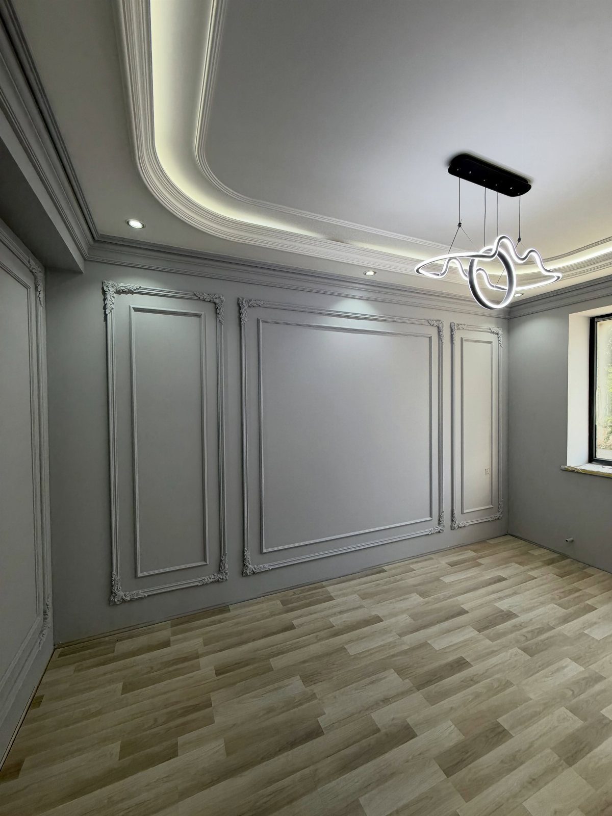 Grey walls with decorative picture frame molding in a modern room with wood flooring.
